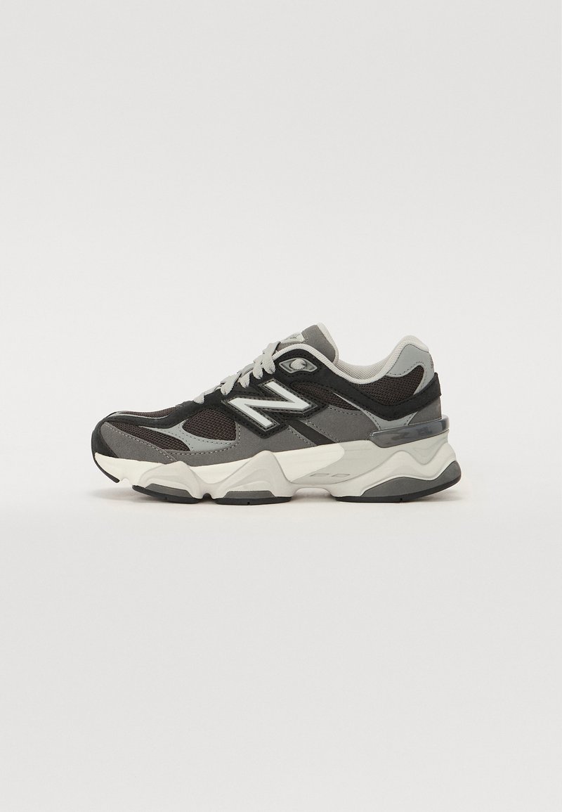 Scarpe sportive con una combinazione di colori nero, grigio e bianco. Presentano materiali in mesh e suede, una suola intermedia spessa e un marchio prominente sul lato.