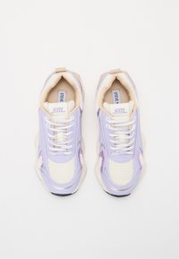Zapatillas moradas y crema con paneles de malla, punta redondeada y suela gruesa. Presentan cordones blancos y una marca en la lengüeta.