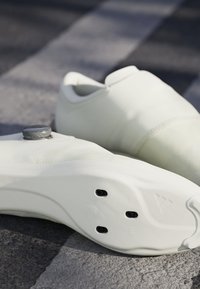 Weiße Sportschuhe mit einem eleganten Design, strukturiertem Obermaterial, runder grauer Hardware oben und einer soliden Sohle mit schwarzen Belüftungsöffnungen.