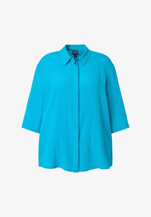 Kirkkaan sininen, löysä naisten paita, jossa on kolme neljänneksen hihaa, terävä kaulus ja edessä piilotettu napitus.