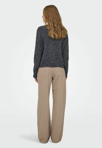 Sivi pleteni džemper s okruglim izrezom uparen s taupe širokim hlačama s bijelim točkicama. Mekana tekstura i ležeran dizajn.