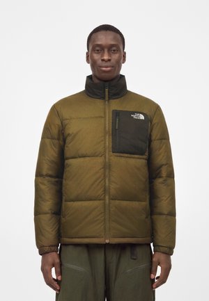 Mann trägt eine olivgrüne gesteppte Jacke mit einer schwarzen Brusttasche mit Reißverschluss und dem The North Face Logo auf weißem Hintergrund.