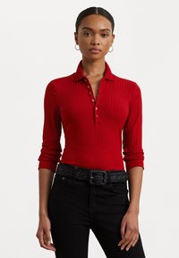 Red ribbed polo shirt with long sleeves and buttoned collar. Paired with a black textured belt and dark jeans. Simple, fitted design.