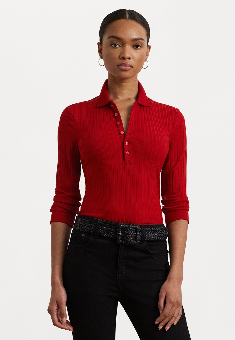 Red ribbed polo shirt with long sleeves and buttoned collar. Paired with a black textured belt and dark jeans. Simple, fitted design.