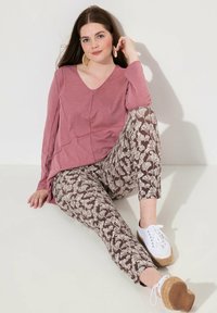 Top a maniche lunghe color rosa con scollatura a V, abbinato a leggings marroni con motivi a foglia bianchi, e scarpe espadrillas bianche.