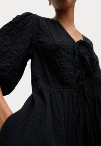 Schwarzes, strukturiertes Kleid mit V-Ausschnitt, Puffärmeln, verstellbarem Bindedetail und gerafftem Rock. Weicher Stoff.