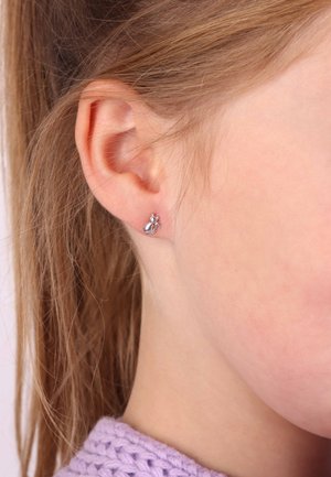 Silbernes, katzenförmiges Steckerearring am Ohrläppchen, mit glatter Textur und minimalistischem Design, getragen von einer Person mit langen, hellbraunen Haaren.