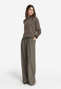 Brun stickad tröja i kombination med högmidjade, plisserade grå byxor. Tröjan har rund halsringning och långa ärmar.