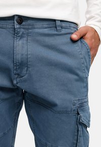 Blå cargo-bukser lavet af blød denim, med lommer, knaplukning og synlige sømme. Mellemhøj talje med et afslappet design.