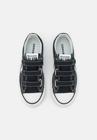 Svarte kanvas-sneakers med hvite gummisåler, med borrelåsstropper, kontrasterende sømmer og klassisk Converse All Star-merke.