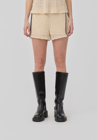 Beige Shorts mit Spitzendesign und lockerer Passform, kombiniert mit kniehohen schwarzen Lederstiefeln mit dicker Sohle.