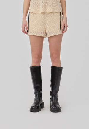 Lace textured beige shorts with a loose fit, paired with knee-high black leather boots featuring a chunky sole.