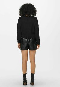 Pull noir en maille avec une coupe ample, associé à un short en similicuir noir brillant. Le mannequin porte des bottines noires. Fond blanc uni.