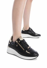 Zapatillas negras de cuero perforado, con detalles en dorado, parte frontal con cordones, cremallera lateral y suela blanca gruesa.