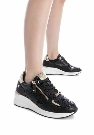 Zapatillas negras de cuero perforado, con detalles en dorado, parte frontal con cordones, cremallera lateral y suela blanca gruesa.