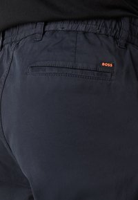 Mörkblå byxor i mjukt tyg, med elastisk midja, bakficka och en liten röd "BOSS"-logotyp.