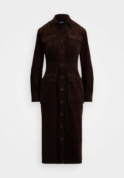 Vestido camisola de veludo cotelê castanho com botão frontal, dois bolsos no peito e dois bolsos laterais. Mangas longas com punhos abotoados.