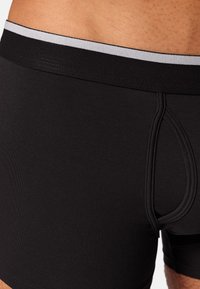 Boxer shorts noirs en tissu lisse, avec une taille grise et un design en poche. Minimalistes et ajustés, sans motifs.