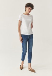Bílý top s krátkým rukávem a čtvercovým výstřihem, spárovaný s modrými skinny džíny. Hnědé semišové baleríny s špičatou špičkou dotvářejí celý outfit.