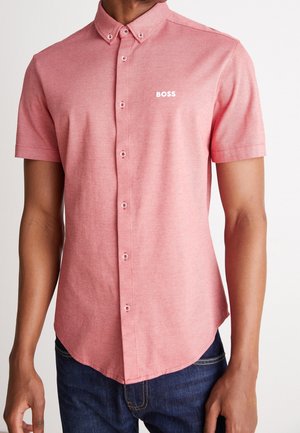 Mand iført en kortærmet, knappet, lyserød skjorte med knaplukning på kraven og hvid "BOSS"-logo på venstre bryst.