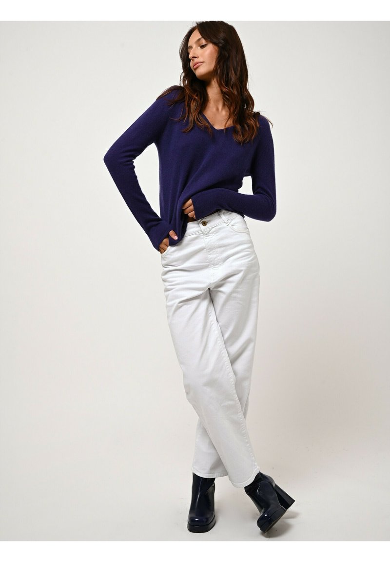 Maglione lavorato a maglia blu navy con maniche lunghe, abbinato a pantaloni bianchi a vita alta. Il modello indossa stivali neri con tacco alla caviglia. Sfondo semplice.