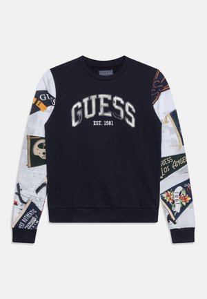 Sweatshirt noir avec des manches contrastées blanches à motifs ; présente le logo "GUESS" et "EST. 1981" en argent. Tissu doux, poignets côtelés.