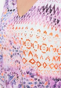 V-Ausschnitt-Top mit einem mehrfarbigen Muster in lila, orange und weiß, verziert mit Pailletten in verschiedenen Größen und geometrischen Designs.