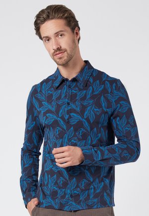 Camisa abotonada de tela azul marino con un patrón botánico de hojas azules. Presenta un cuello clásico y mangas largas, con una textura suave en toda la prenda.