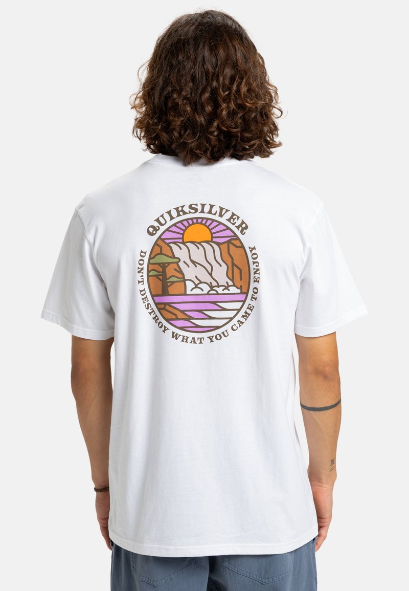 T-shirt de algodão branca com uma gráfica colorida de um pôr-do-sol, cachoeira e árvore, com o texto "Quiksilver" e um slogan nas costas.
