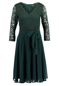Mörkgrön klänning med spetsliv, V-ringning och trekvartslång ärm. Luftigt tyg och ett matchande bälte knutet i midjan.