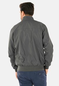 Giacca bomber grigia realizzata in materiale leggero e morbido, con vita e polsini a costine, dotata di un colletto alto e senza decorazioni visibili.