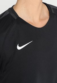 Czarna koszulka sportowa z krótkimi rękawami, okrągłym dekoltem i gładką fakturą. Posiada białe logo Nike w kształcie łuku na piersi.