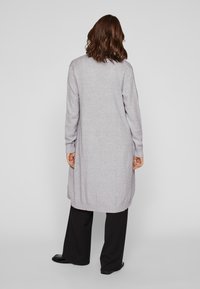 Hallilong kootja, millel on mugav lõige, soonikkoes mansetid ja ääred, valmistatud pehmest kudumist, kombineeritud vaba mustade pükstega.