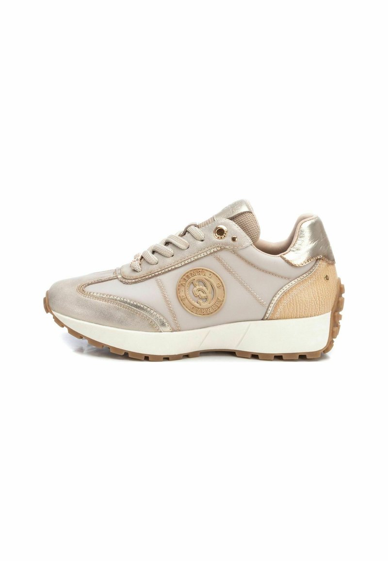 Zapatilla deportiva beige con acentos metálicos, revestimiento texturizado y detalle del logo. Presenta una suela blanca gruesa y una banda de goma para mayor tracción.