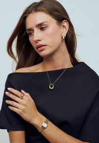 Guldsmycken som inkluderar ett hängande halsband, creoler och en iögonfallande ring, tillsammans med en silverfärgad klocka med en rektangulär urtavla.