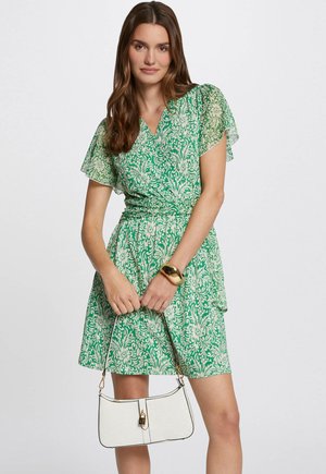 Green floral patterned dress with sheer flutter sleeves and a cinched waist. Accompanied by a white handbag with gold hardware and a smooth texture.