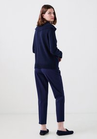 Granatowy sweter dzianinowy z szerokim kołnierzem, zestawiony z dopasowanymi granatowymi spodniami i płaskimi mokasynami. Gładka tekstura z subtelnymi detalami.