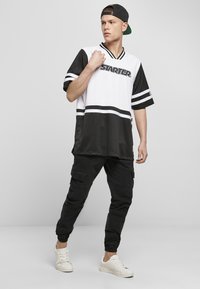 Hvid og sort kortærmet trøje med "STARTER" logo, striped dekor, sammen med sorte cargo bukser og hvide sneakers.