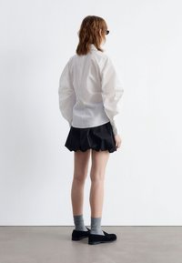 White long-sleeve shirt with puffed sleeves, paired with a black ruffled skirt. Black shoes and gray socks complete the outfit.