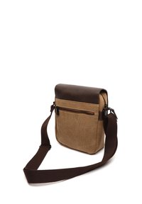 Bolso cruzado de lona color arena con solapa de cuero sintético marrón, correa ajustable, bolsillo frontal con cremallera y superficie texturizada.