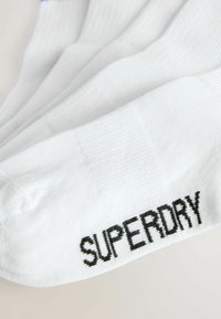 Valged spordisokid ribakujundusega, mille pealt on õmmeldud must "SUPERDRY" logo. Sile kangas tugevdatud kanna ja varbaga.