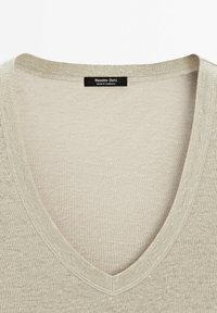 Jasnobeżowy sweter z dekoltem w serek o gładkiej fakturze. Posiada prążkowany kołnierz. Etykieta z napisem "Massimo Dutti, Made in Cambodia."
