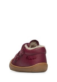 Scarpina per bambini in pelle bordeaux con un cinturino in velcro, morbido rivestimento interno e suola in gomma texturizzata. Presenta una punta arrotondata e un branding minimo.