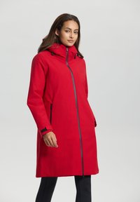 Manteau long imperméable rouge avec un col haut, une fermeture éclair à l'avant et des poches latérales. Présente des accents noirs et des cordons de serrage ajustables sur la capuche.