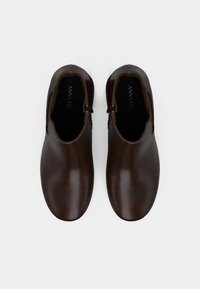 Brūni ādas apavi ar gludu virsmu, ar noapaļotu purngalu un mazu sānu atvērumu. Iekšpusē ir melna oderes ar zīmola nosaukumu.