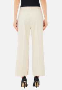 Pantaloni beige a gamba larga con una texture liscia, design a vita alta e due tasche posteriori, abbinati a tacchi alti neri.