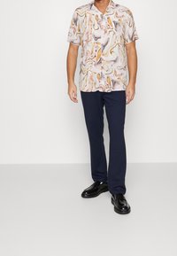 Camicia a maniche corte con un motivo marmorizzato colorato in rosa, arancione e crema, abbinata a pantaloni blu scuro e scarpe nere.