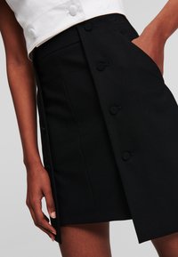 Svart kjol med skräddarsydd design, har en sidficka och dekorativa knappar framtill. Slätt tyg med en ren, minimalistisk look.