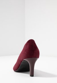 Burgundyröd mockaskor med hög klack, spetsig tå och medelhög klack. Har en slät yta och en enkel, strömlinjeformad design.