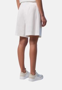 Pantaloni corti bianchi in lino dalla vestibilità ampia, caratterizzati da una linea dritta e una cintura elastica, abbinati a sneakers di colore chiaro.